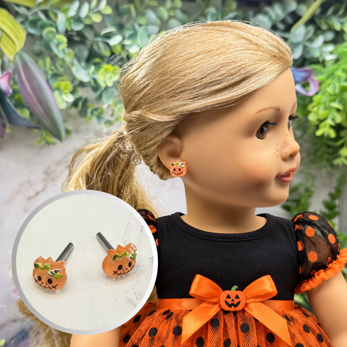 A doll with blonde hair wearing a black and orange Halloween dress, shown in profile with an inset circle displaying matching pumpkin-shaped stud earrings.