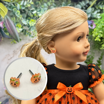 A doll with blonde hair wearing a black and orange Halloween dress, shown in profile with an inset circle displaying matching pumpkin-shaped stud earrings.