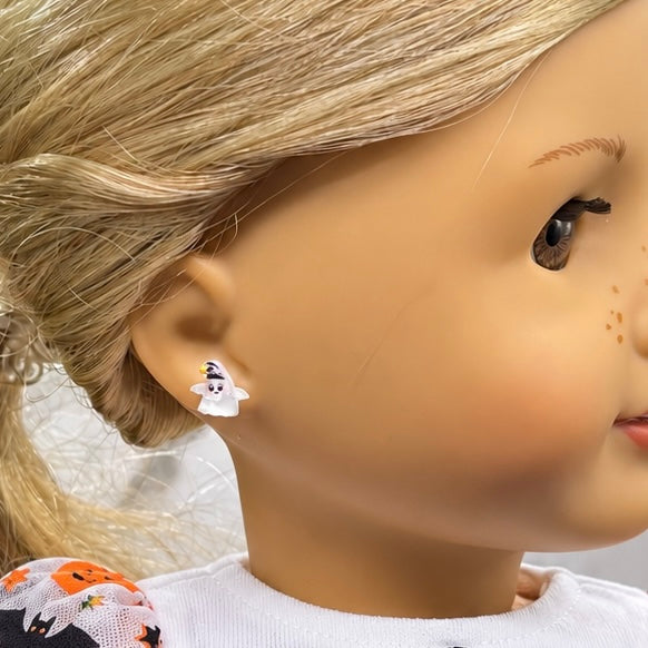 A close-up of a doll's head wearing a small white ghost stud earring with a black witch hat accent.