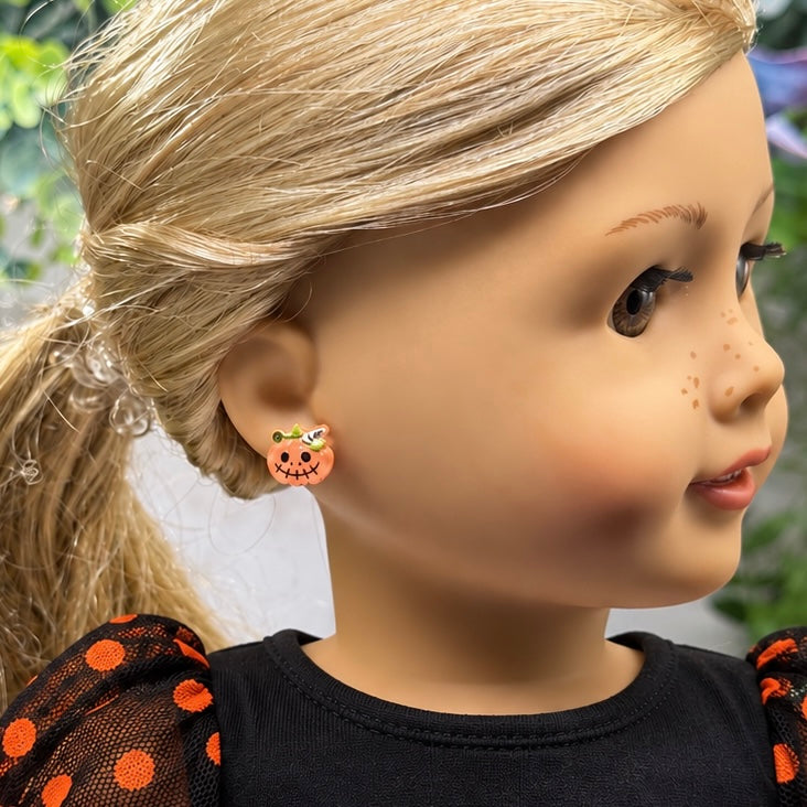 A close-up of a blonde doll wearing a small orange pumpkin-shaped stud earring with a jack-o'-lantern face and tiny green and yellow accents.