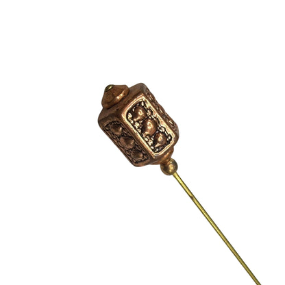 Bronze-colored stickpin with intricate design on a white background