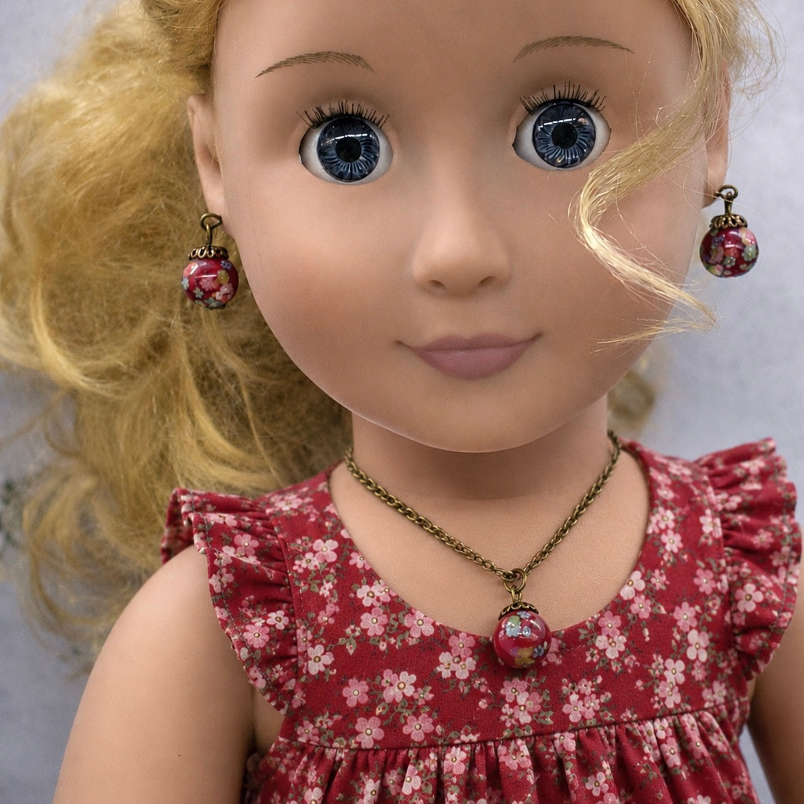 Add a pop of color to your doll's outfit with this Red glass Drop Pendant Doll Necklace Earrings Set. The set includes a red pendant necklace and matching earrings with floral design. The necklace measures 6.5 in length. Necklace and earrings shown on 18" Our Generation doll