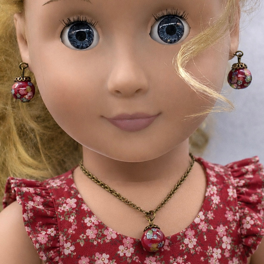 Add a pop of color to your doll's outfit with this Red glass Drop Pendant Doll Necklace Earrings Set. The set includes a red pendant necklace and matching earrings with floral design. The necklace measures 6.5 in length. Necklace and earrings shown on 18" Our Generation doll