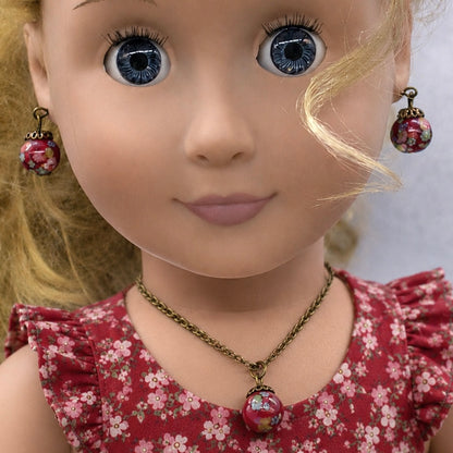 Add a pop of color to your doll's outfit with this Red glass Drop Pendant Doll Necklace Earrings Set. The set includes a red pendant necklace and matching earrings with floral design. The necklace measures 6.5 in length. Necklace and earrings shown on 18" Our Generation doll