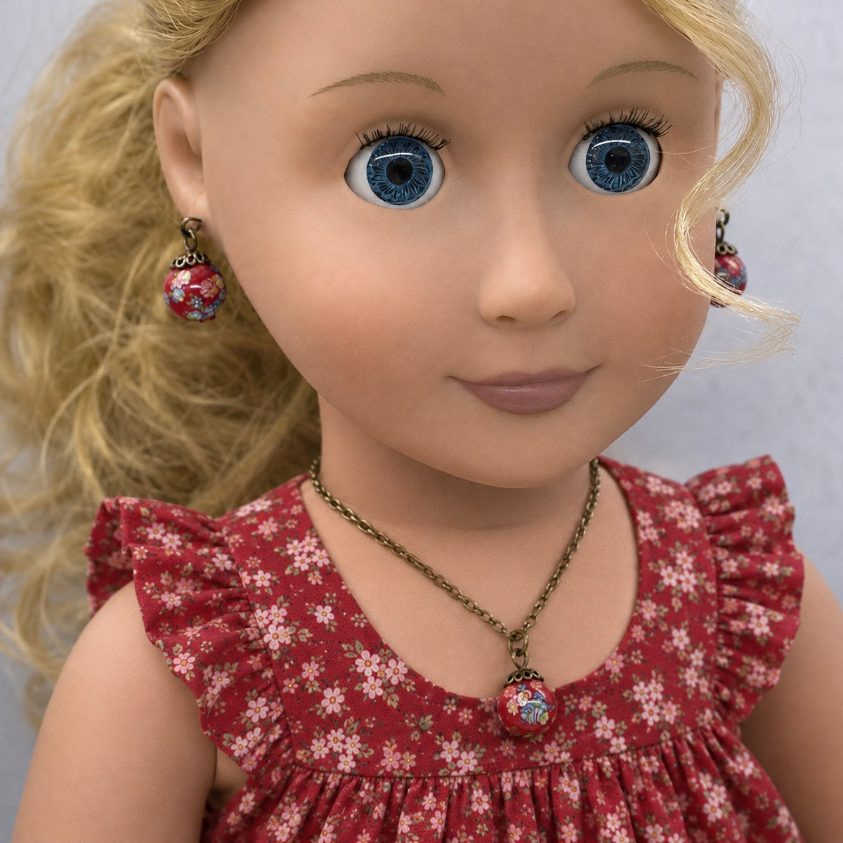 Add a pop of color to your doll's outfit with this Red glass Drop Pendant Doll Necklace Earrings Set. The set includes a red pendant necklace and matching earrings with floral design. The necklace measures 6.5 in length. Necklace and earrings shown on 18" Our Generation doll